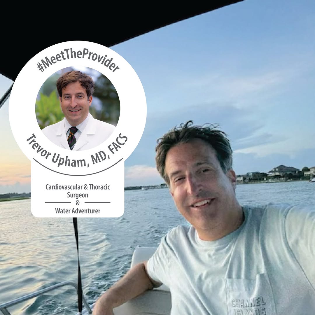 Cardiovascular surgeon Trevor Upham smiling on a boat with calm water and houses in the background at sunset.