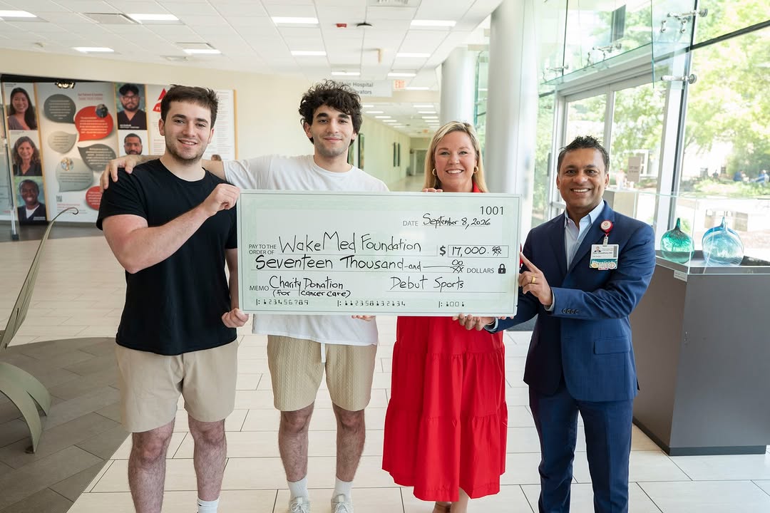 Two young men and two adults holding a large $17,000 donation check for the WakeMed Foundation inside a bright lobby.
