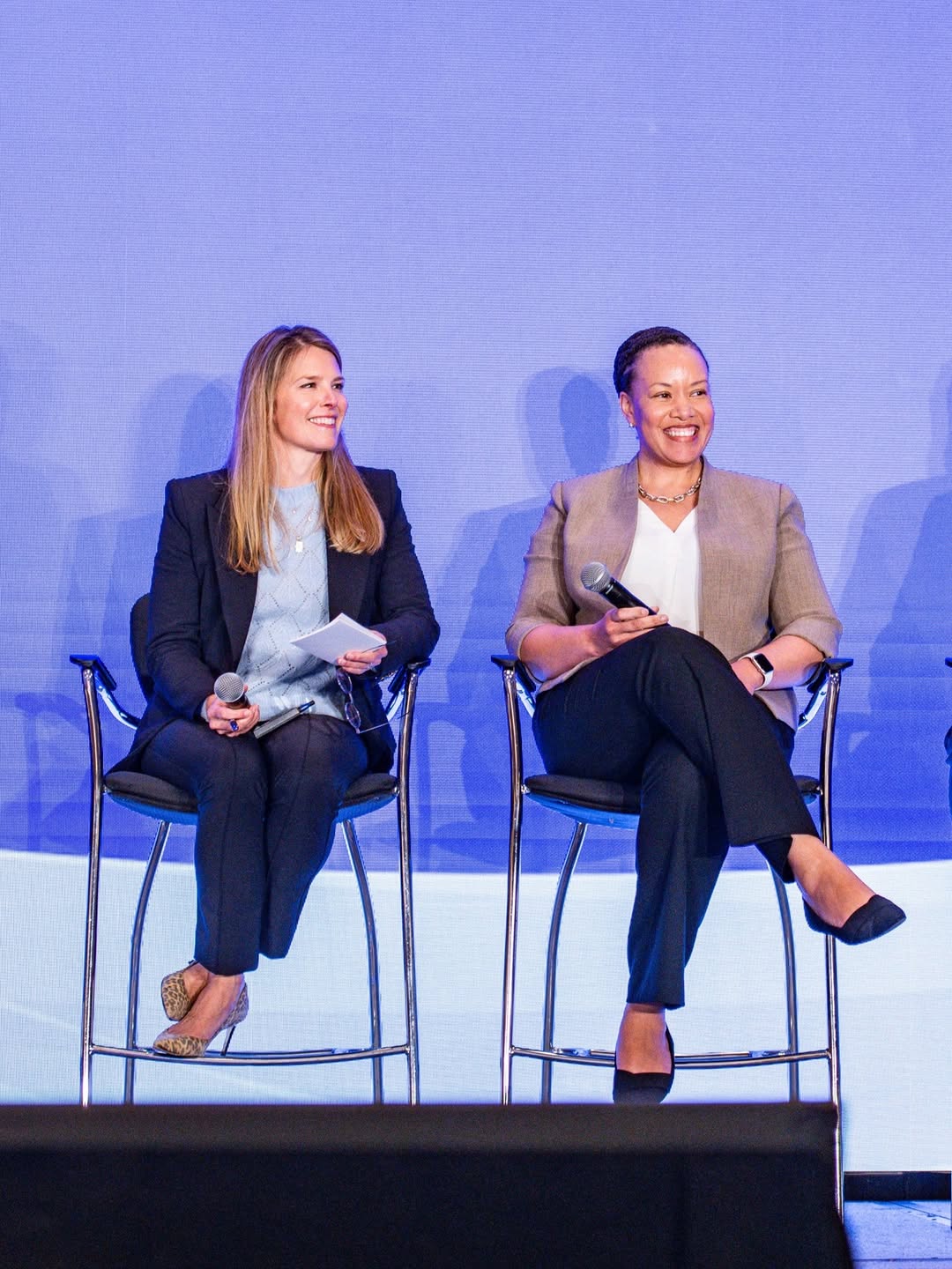 Sentara's four market presidents, from left to right, Jeff Joyner, Joanne Inman, Dana Weston Graves, and Kapua Conley, are seated in tall chairs on a stage, holding microphones, against a blue backdro