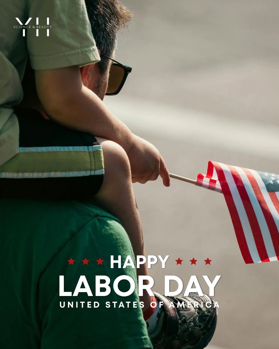 Child on an adult's shoulders holding a small American flag; overlay text: "Happy Labor Day."